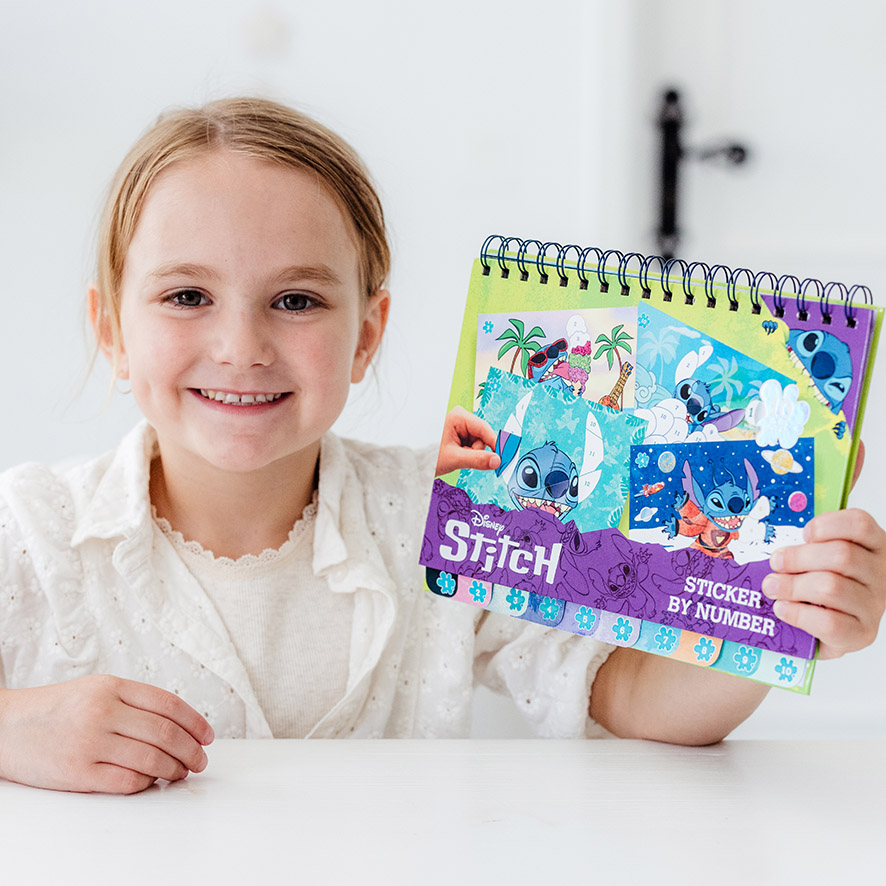Menina feliz a mostrar o livro de atividades Totum Sticker by Number do Stitch, com autocolantes coloridos.