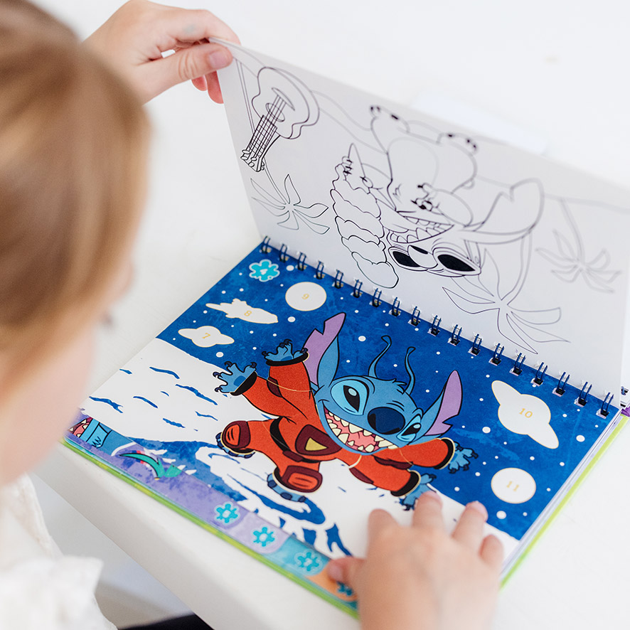 Criança a ver uma página para colorir e uma página de autocolantes por números do Stitch no livro Totum.