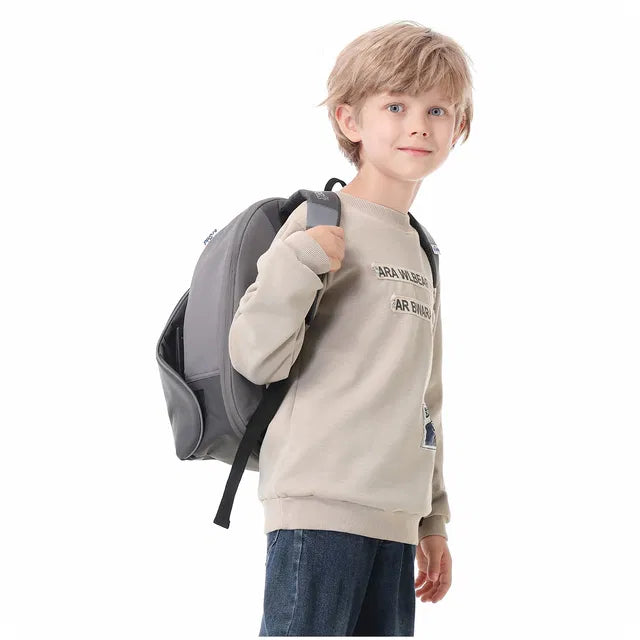 Criança a sorrir enquanto coloca a Trunki BoostApak cinzenta ao ombro como uma mochila.