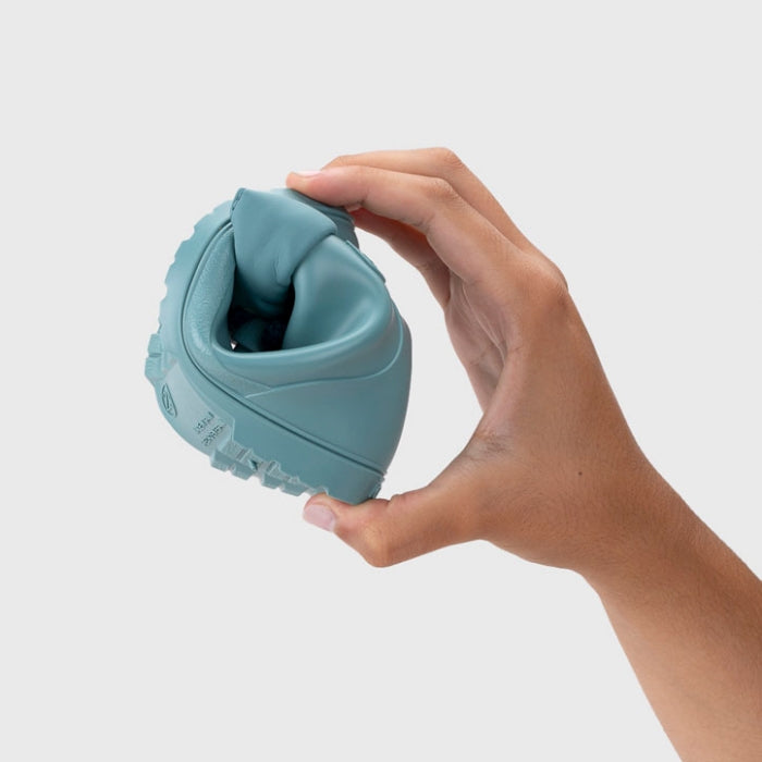 Uma mão a dobrar a galocha Igor MENDI Turquesa, demonstrando a sua extrema flexibilidade e material maleável.