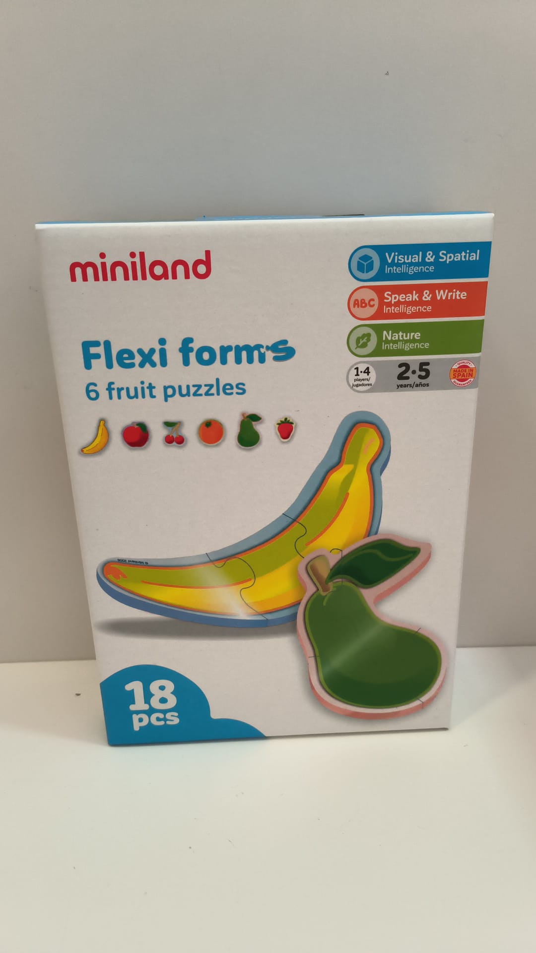 Caixa do puzzle Miniland Flexi forms 6 fruit puzzles, mostrando as frutas banana e pera, com indicações de idade (1-4, 2-5 anos) e 18 peças. Destaca inteligência visual, espacial, fala e natureza.