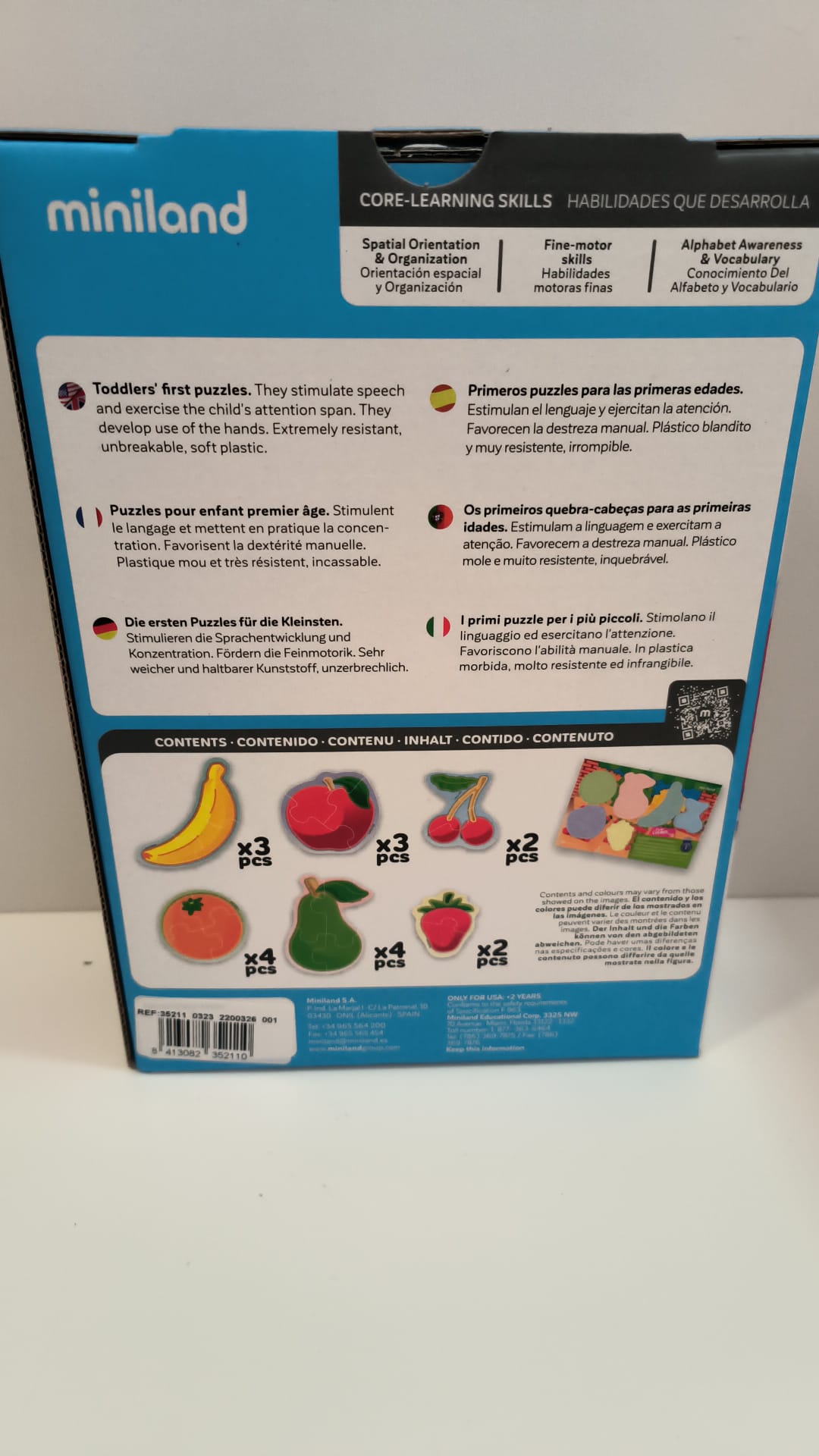 Verso da caixa do puzzle Miniland Flexi forms, detalhando as habilidades desenvolvidas (orientação espacial, motoras finas, vocabulário) e o conteúdo exato das 18 peças de frutas em plástico macio.