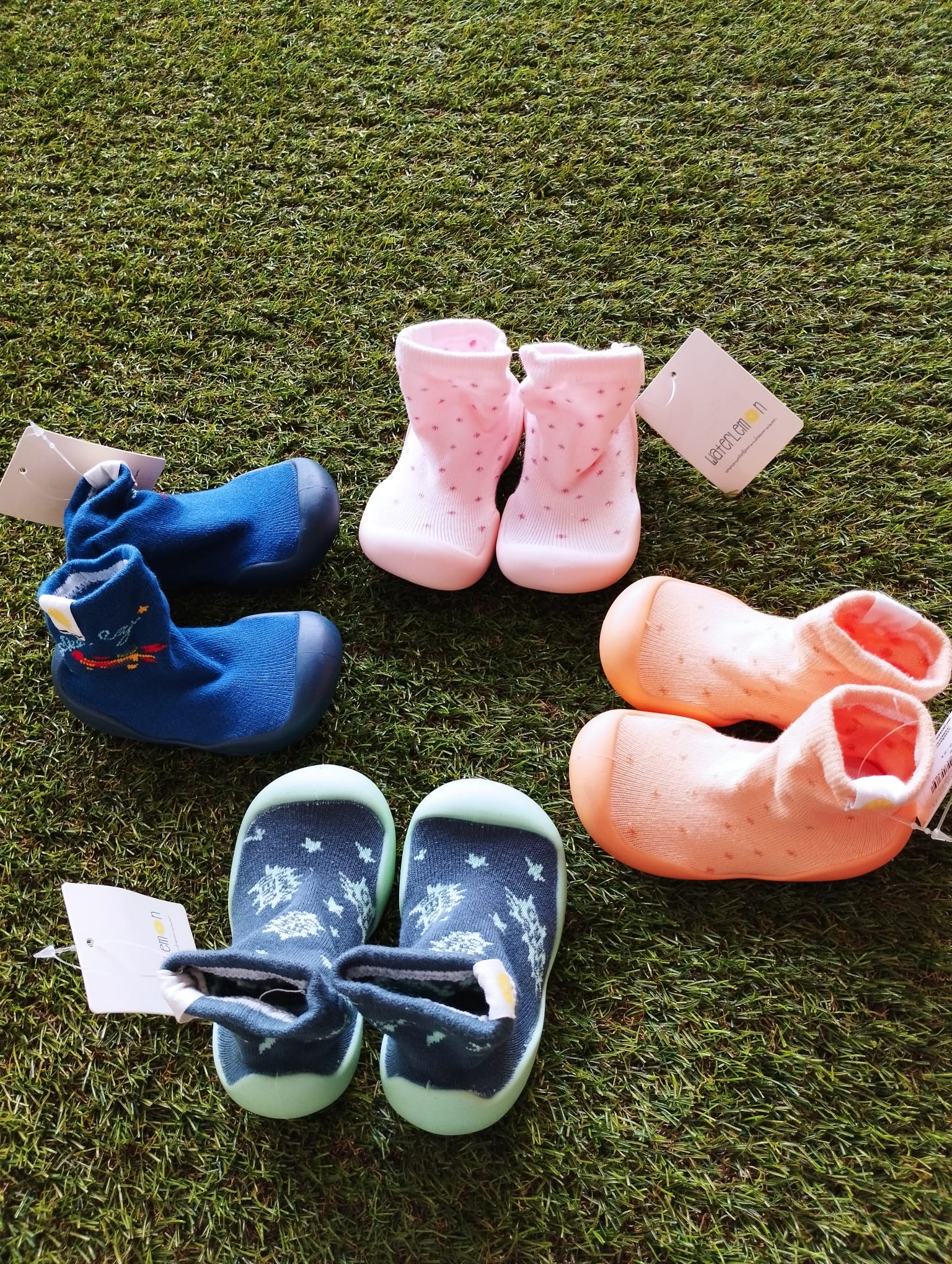 Conjunto de pantufas tipo meia em várias cores, incluindo azul, rosa e laranja, dispostas sobre relva artificial. Opções diversas para diferentes gostos e necessidades.
