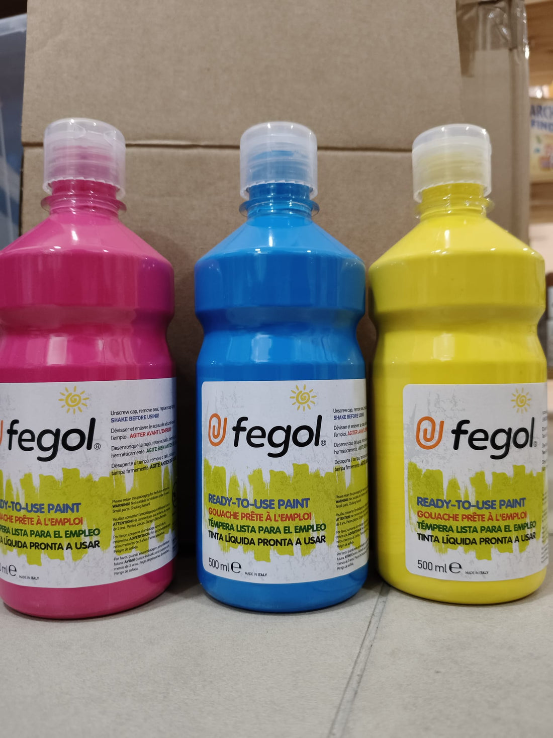 Três boiões de tinta líquida Fegol pronta a usar de 500ml em cores vibrantes: rosa, azul e amarelo, destacando a variedade do produto.