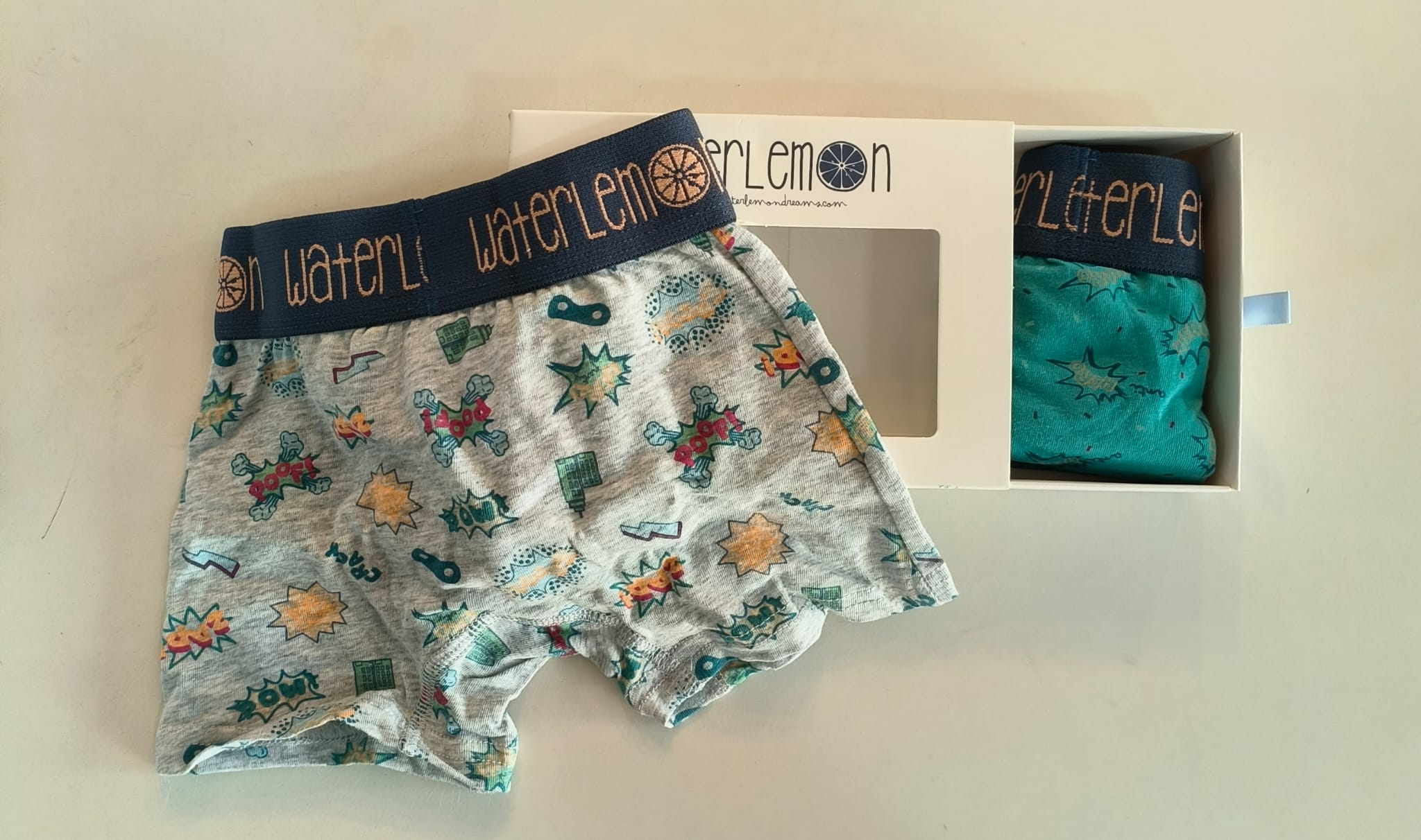 Boxer Waterlemon cinzento com padrão de banda desenhada e uma caixa aberta com outro boxer verde de banda desenhada.