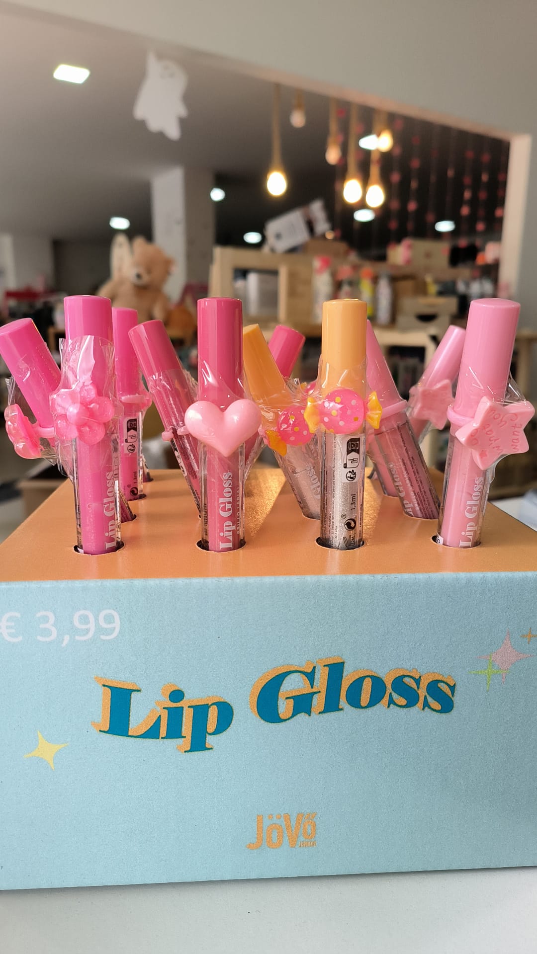 Exposição de vários Lip Gloss Sweet da Jövo em tons de rosa e laranja, com anéis decorativos, num expositor de loja com o preço de 3,99€.