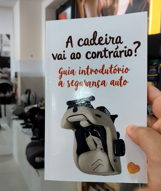 Mão a segurar o guia "A Cadeira vai ao contrário?", exibindo a capa com o título e ilustração de uma cadeira auto virada para trás.