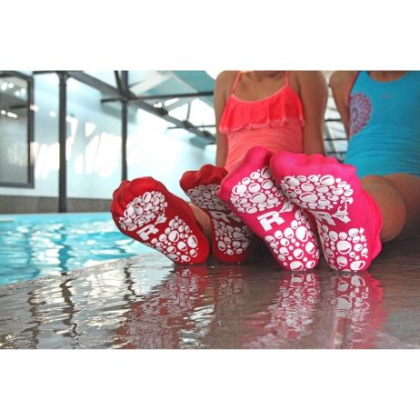 Crianças com meias antiderrapantes Pool Kids na piscina – Duas crianças sentadas à beira da piscina, usando meias antiderrapantes rosa com solado branco texturizado. A água reflete a luz, destacando a segurança e aderência do produto.