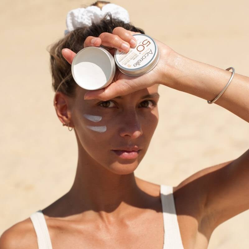 Mulher aplicando protetor solar sólido Acorelle SPF50+ no rosto, demonstrando a facilidade de uso e proteção solar.
