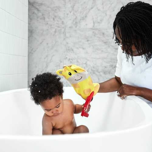 Mãe ou cuidadora a lavar um bebé na banheira com a luva de banho amarela em forma de girafa.