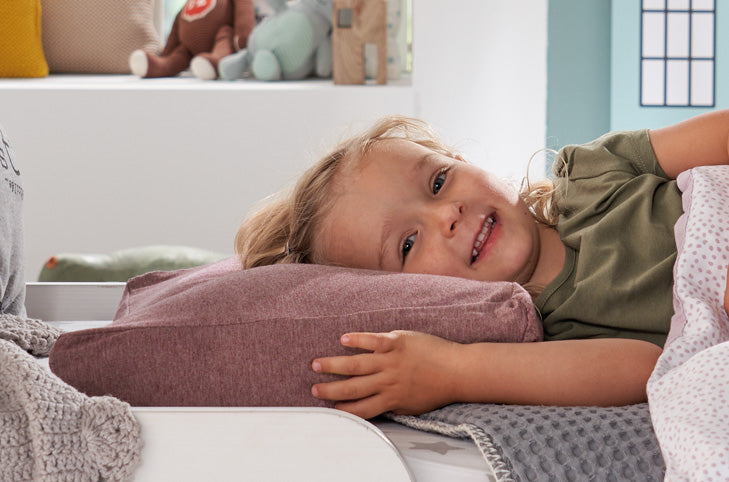 Crianca a sorrir deitada confortavelmente numa almofada Theraline num quarto infantil luminoso