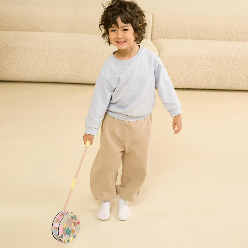 Menino sorridente a brincar e a andar com o Classic World Rolo Arco Íris de empurrar numa sala de estar.