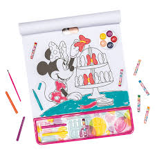 Bloco de desenho aberto com Minnie Mouse a colorir um bolo, rodeado por lápis de cera, pincel e aguarelas.