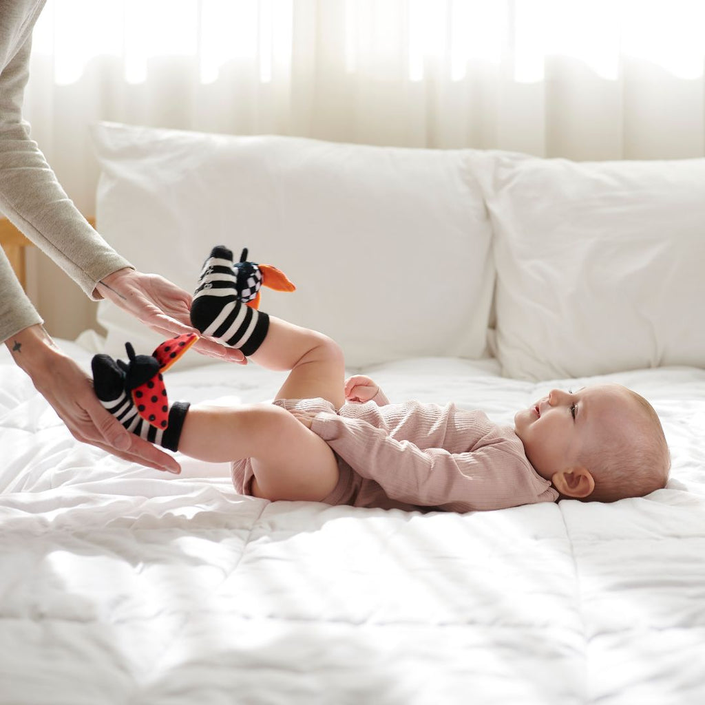 Bebé a usar meias Attipas ATTISOCKS coloridas, com solas antiderrapantes visíveis, a brincar no chão.