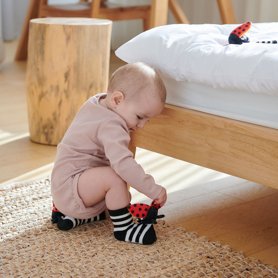 Bebé a explorar uma superfície com as meias Attipas ATTISOCKS, destacando a flexibilidade e a estimulação sensorial proporcionada pelo produto.