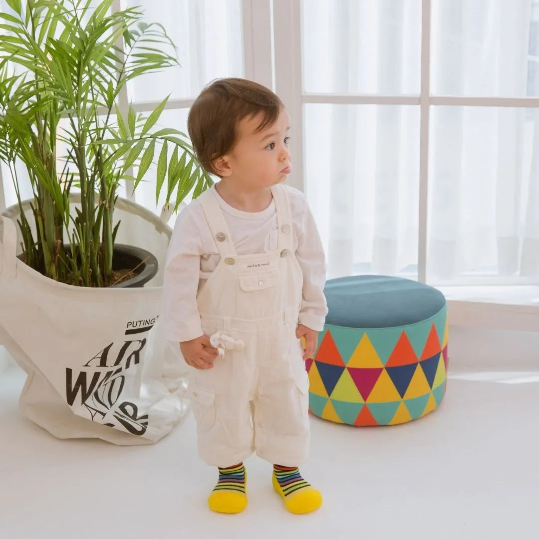 Attipas Rainbow Yellow, calçado barefoot infantil com riscas coloridas e sola amarela antiderrapante, leve, flexível e confortável para os primeiros passos.