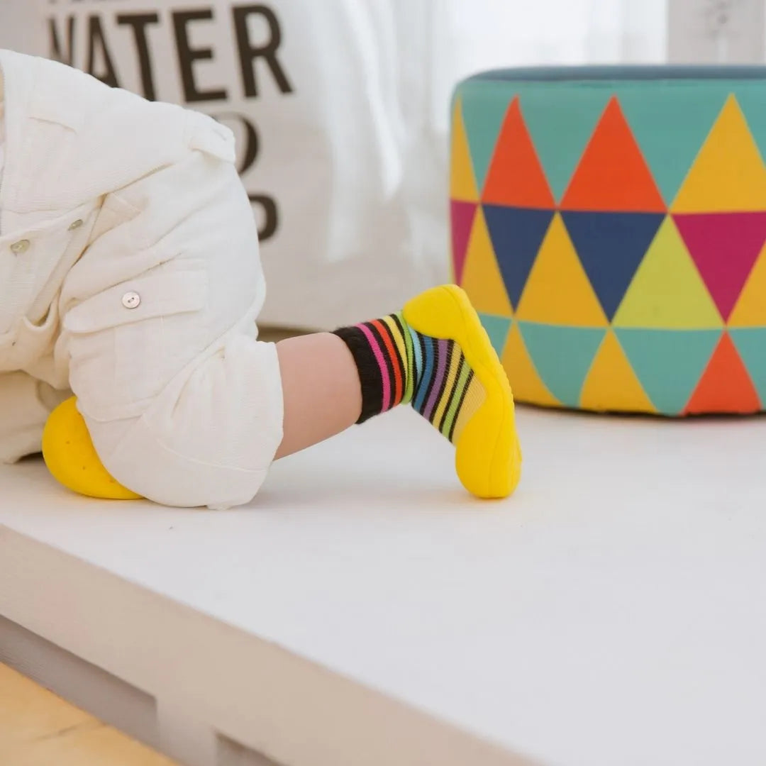 Bebé a gatinhar com Attipas Rainbow Yellow, evidenciando a flexibilidade e o ajuste ergonómico ao pé.