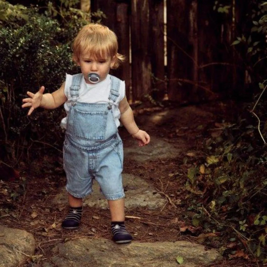 Criança de macacão azul a caminhar na natureza, usando Attipas Hedgehog Navy, demonstrando liberdade de movimentos.
