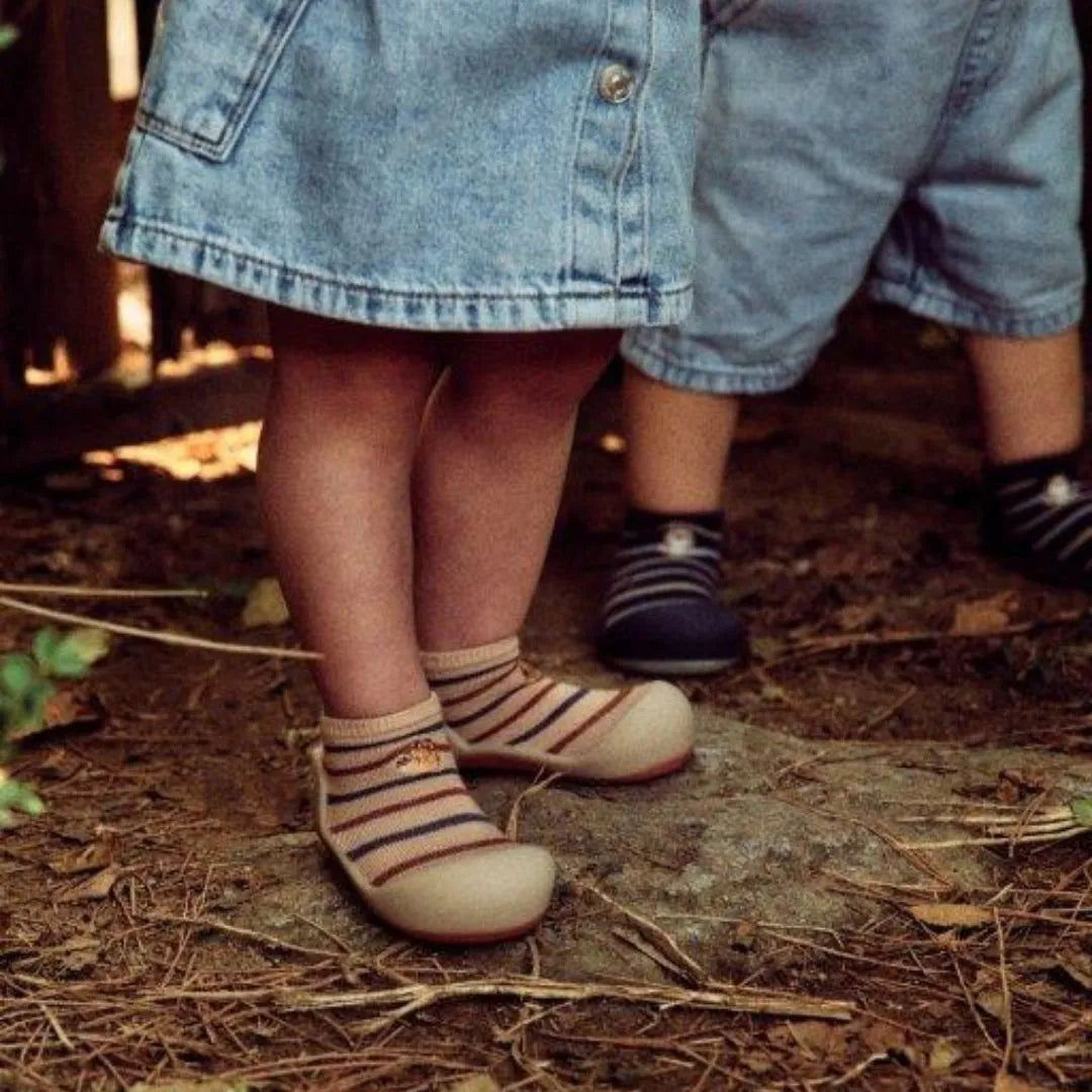 Criança a usar Attipas Sloth Beige, caminhando ao ar livre sobre solo irregular, demonstrando o conforto e aderência do calçado.