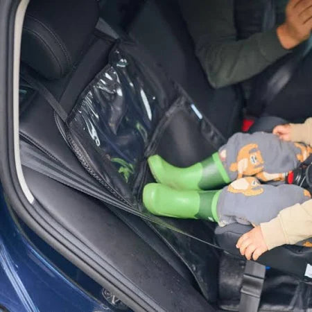 Instalação da capa protetora Axkid no banco traseiro de um carro, protegendo contra botas verdes de criança que tocam no encosto.