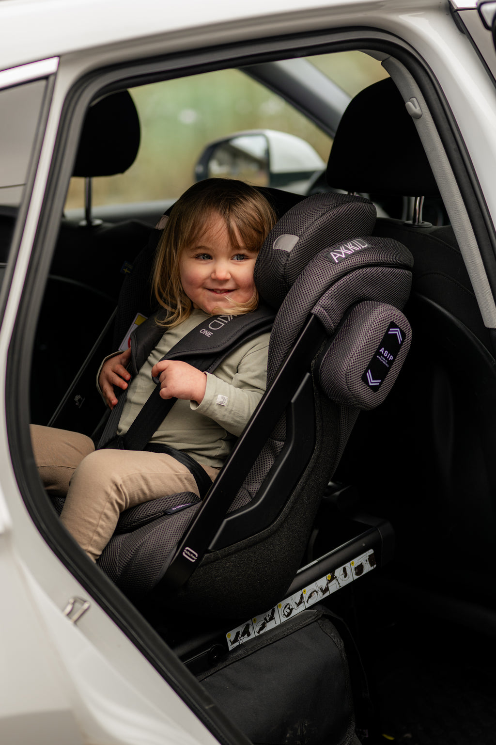 Crianca feliz a ajustar o cinto da cadeira auto Axkid ONE 3 Mesh.