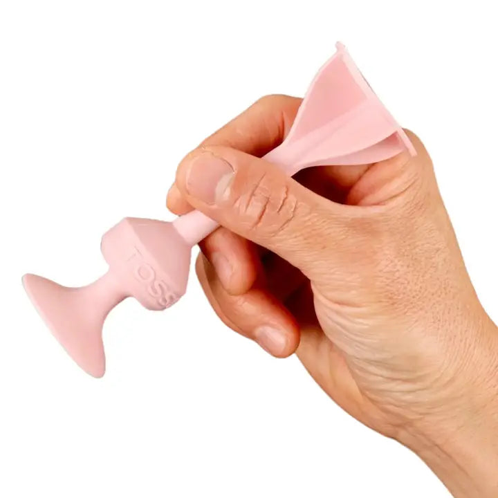 Mão a segurar um dardo TOSSIT cor-de-rosa, demonstrando a sua forma e a ventosa na base.