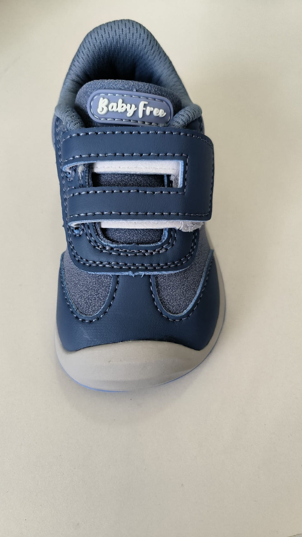 Vista frontal da sapatilha barefoot azul, focando nas duas tiras de velcro e na etiqueta "Baby Free" na lingueta.