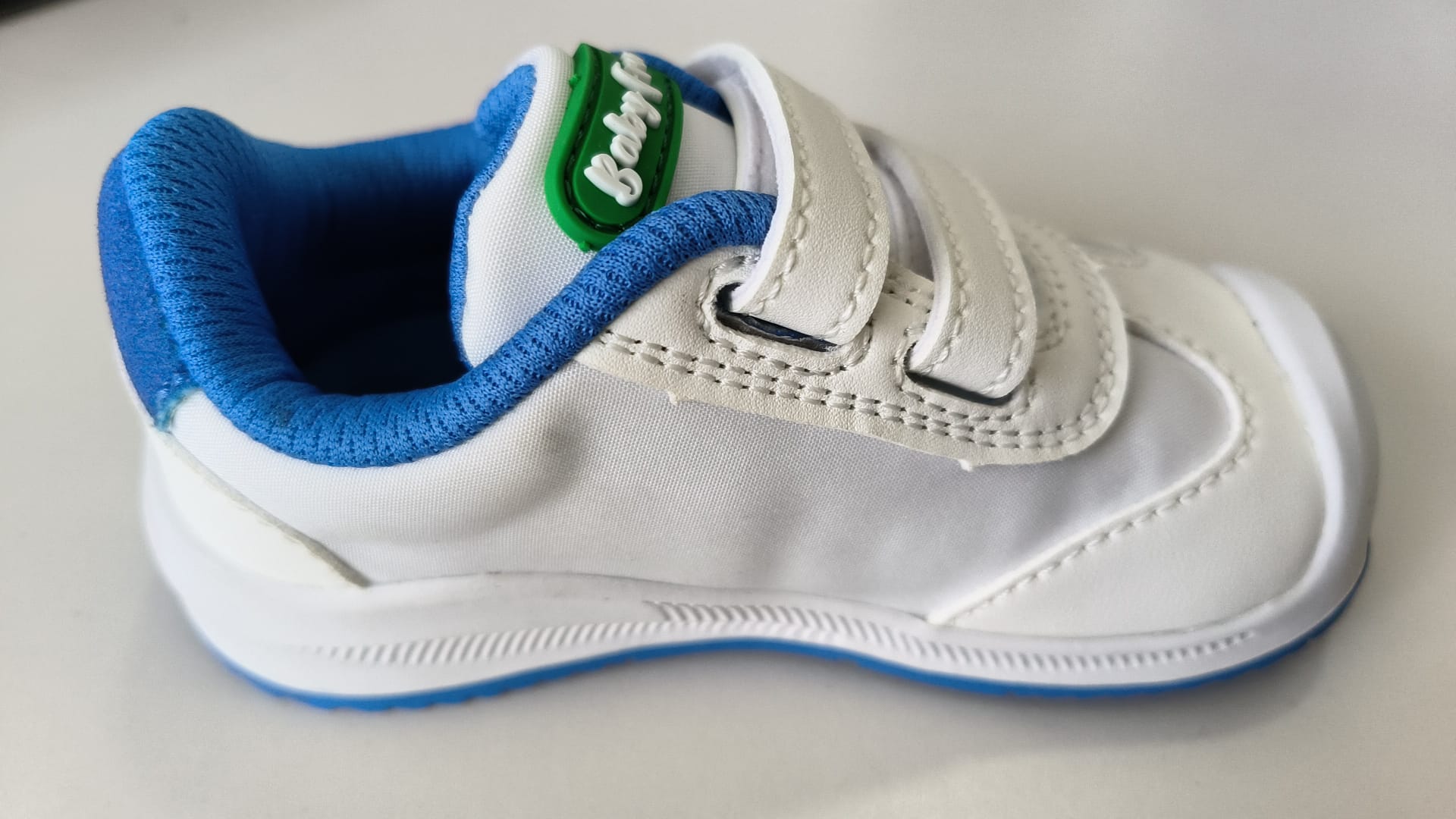 Sapatilha BabyFree Barefoot branca e verde com detalhes em azul, mostrando a flexibilidade e o sistema de fecho prático com tiras aderentes.