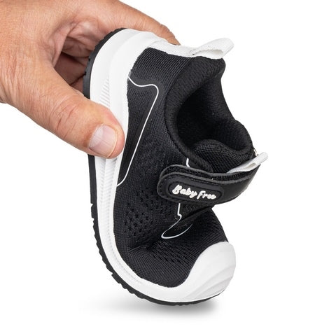 Mão a dobrar a sapatilha BabyFree Barefoot negra, demonstrando a extrema flexibilidade do calçado respeitador.