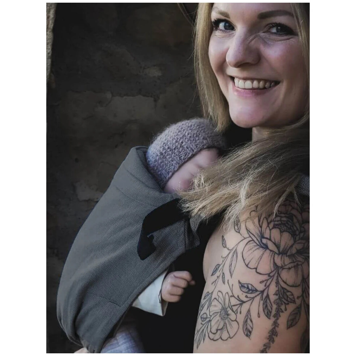 Mãe a carregar bebé recém-nascido de forma ergonómica em mochila Hoppediz cinzenta.
