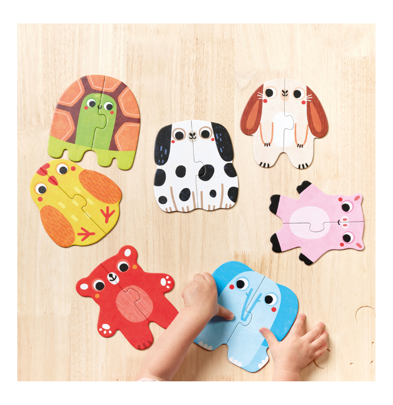 Mãos de uma criança a montar os puzzles de animais em cima de uma superfície de madeira clara, com seis peças já separadas e uma a ser encaixada.