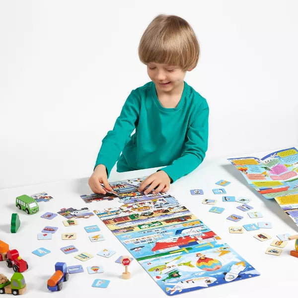 Criança a montar o Puzzle Transporte Banana Panda numa mesa, rodeado por peças, cartões e pequenos veículos de madeira.