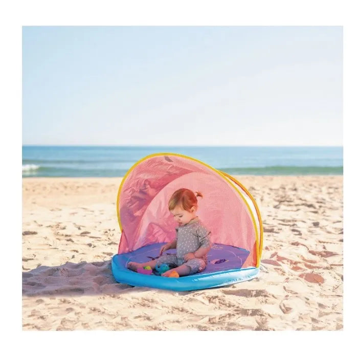 Bebé a brincar na tenda Olmitos Deep Blue na praia, com o mar azul ao fundo.