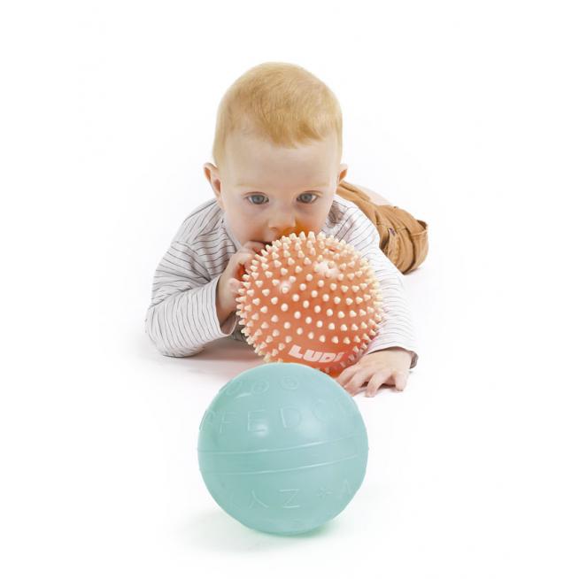 Bebé a explorar uma bola sensorial laranja com pontas, com uma bola azul ao lado.