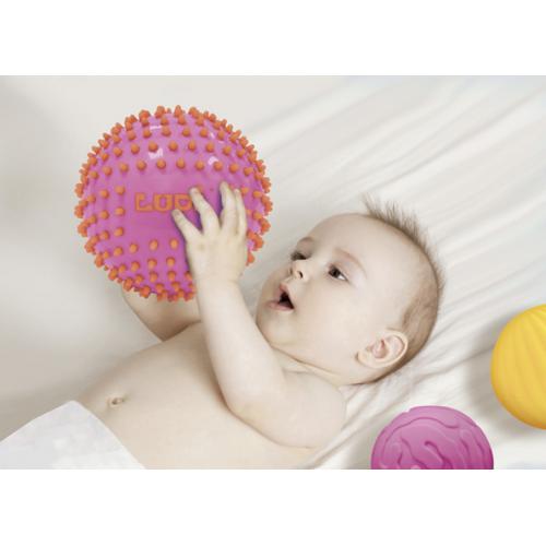 Bebé deitado a segurar uma bola sensorial rosa com espinhos macios.