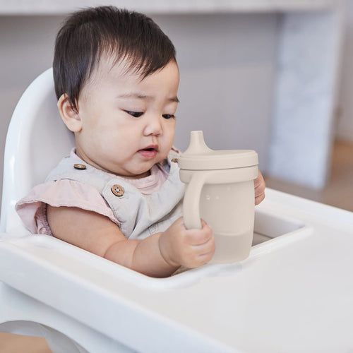 Bebé sentado numa cadeira alta a beber de um copo de silicone b.box Latte com alças e tampa.