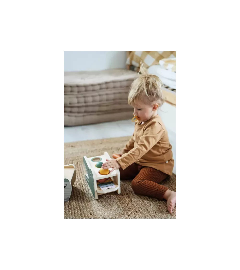 Criança pequena brincando com o jogo de martelar e xilofone small foot, focada na interação com o brinquedo.