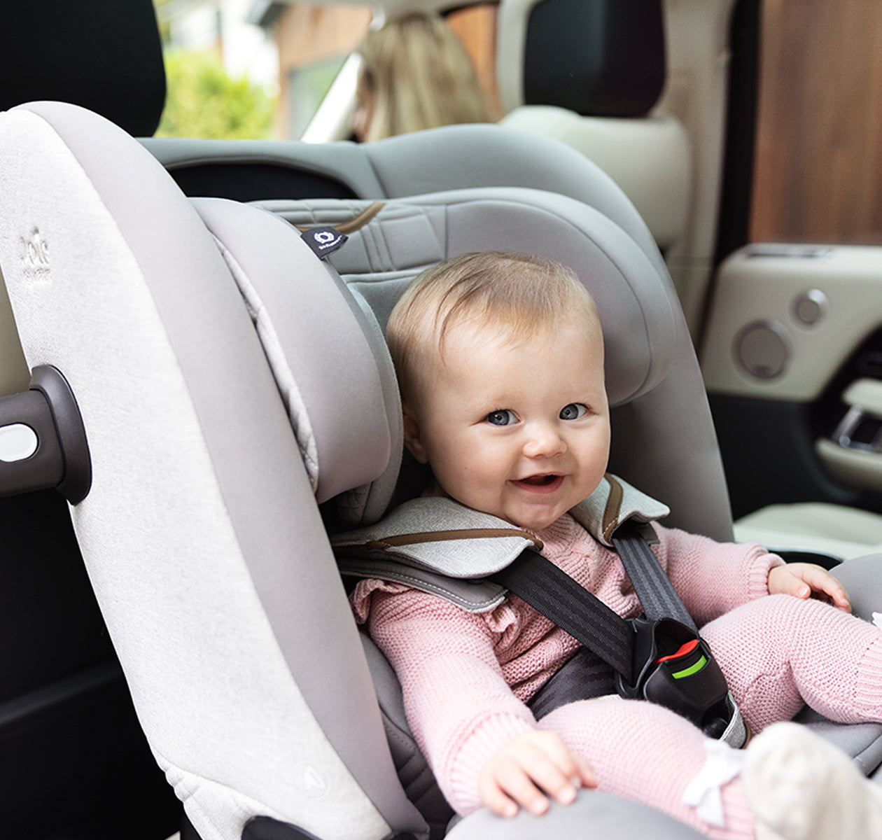 Bebé sorridente sentado confortavelmente na cadeira auto Joie i-Spin XL Signature instalada no carro, em posição contra marcha.