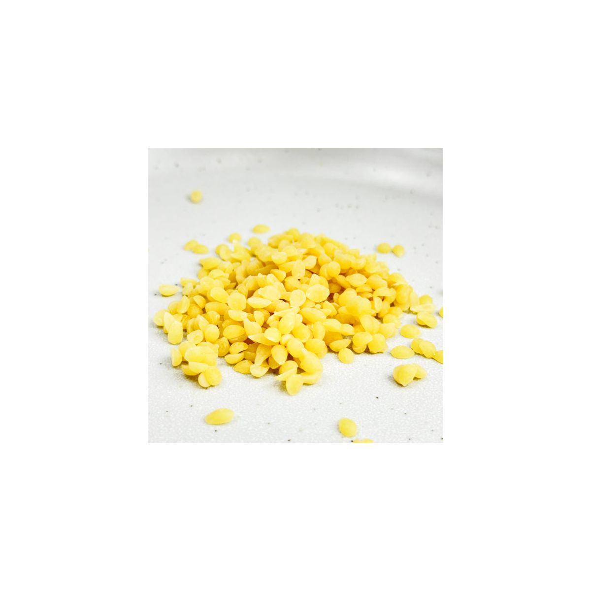 Close-up detalhado de um monte de pérolas de cera de abelhas certificada orgânica de cor amarelo natural, mostrando a sua textura e forma uniforme.