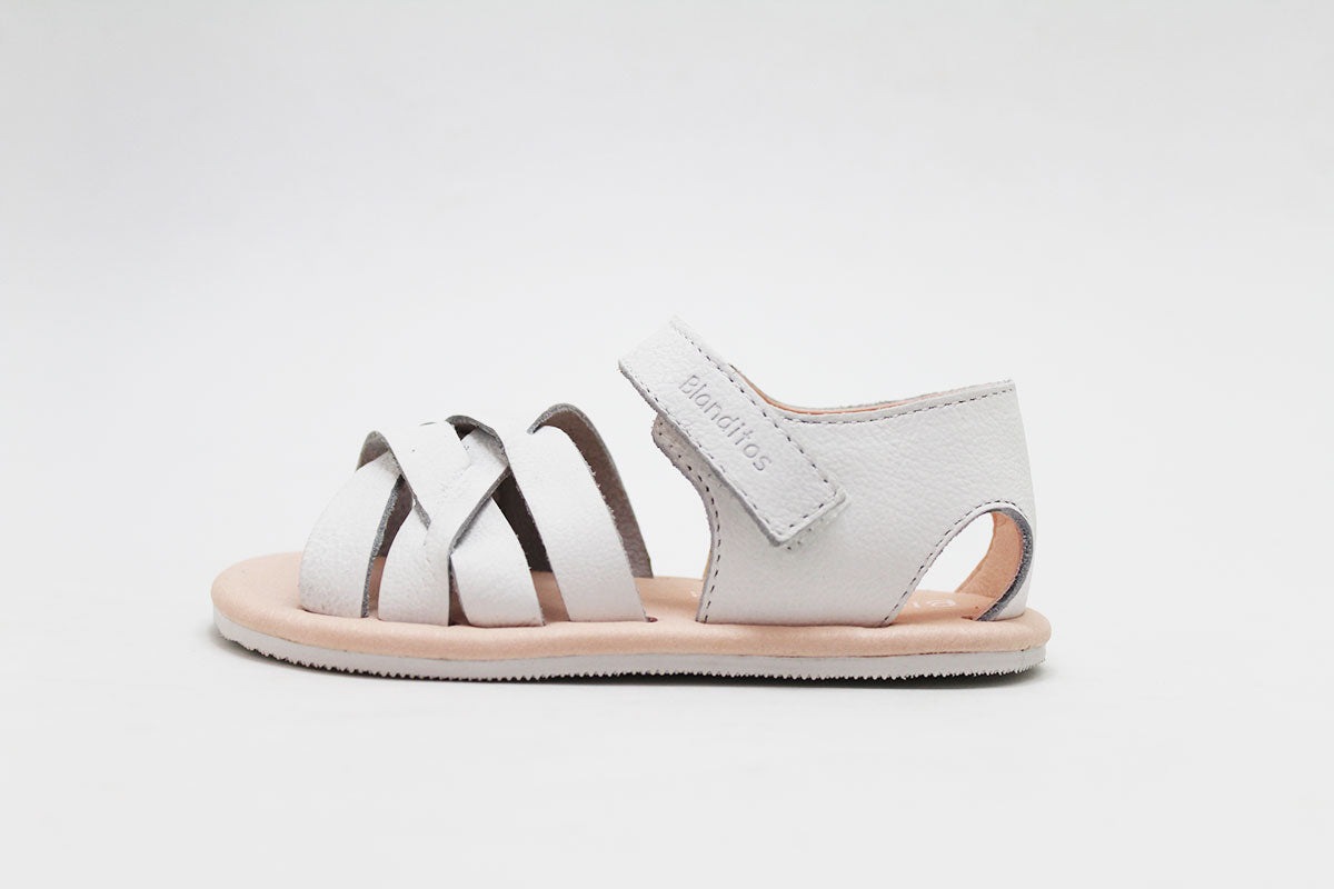 Vista lateral detalhada da sandália infantil Blanditos by Crio's em pele branca, mostrando a sola fina e o design aberto.