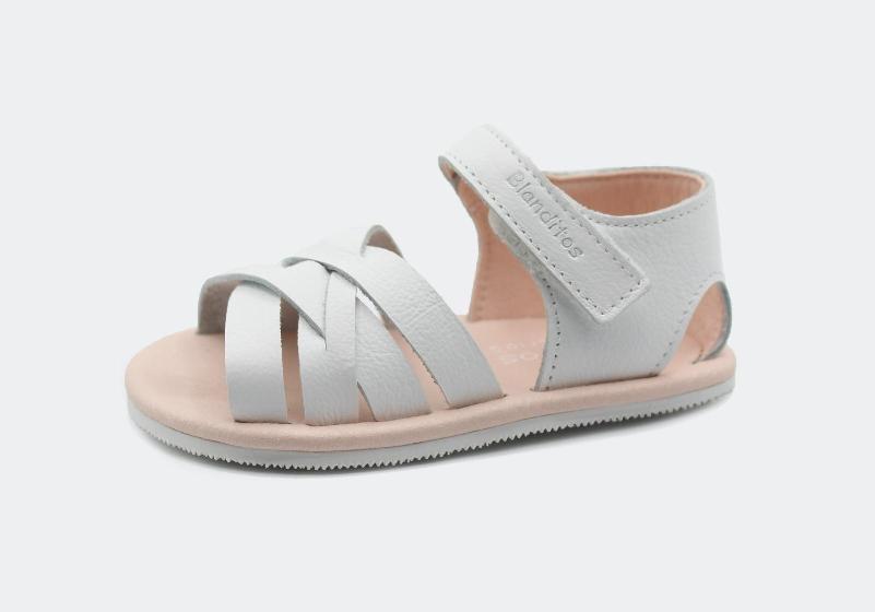 Sandália infantil aberta Blanditos by Crio's em pele branca com tiras entrelaçadas e fecho de velcro. Fundo cinza claro.