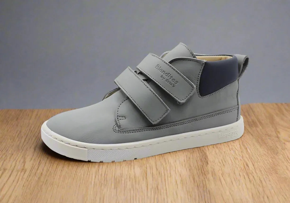 Sapatilha Blanditos Etna cor Gris (cinza) sobre superfície de madeira, vista de perfil. Calçado Barefoot infantil com sola branca, flexível e fecho duplo de velcro.