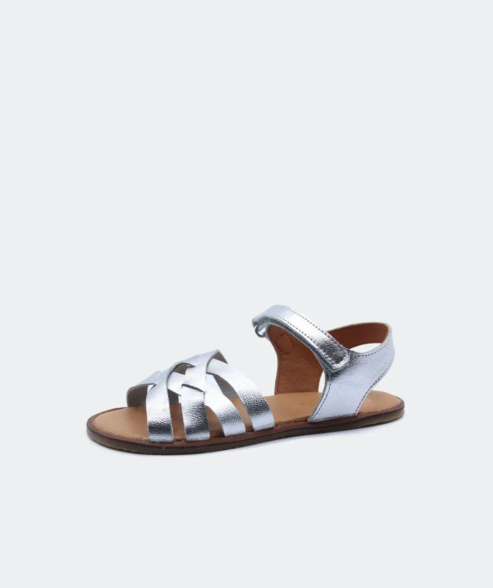 Sandália Blanditos Ithaca em prata, com acabamento metálico, tiras cruzadas de couro natural e sola fina para uma experiência barefoot.