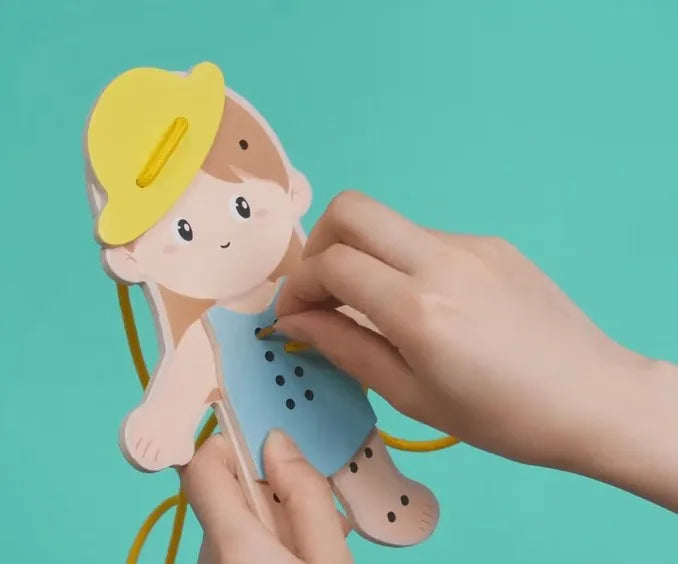 Mãos de criança a enlaçar um vestido na figura de menina do brinquedo Classic World, mostrando a atividade.