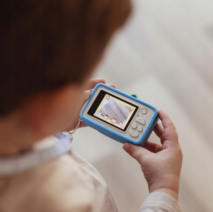 Criança a usar a máquina fotográfica Hoppstar Rookie Bluebelle, mostrando o ecrã com filtros e molduras divertidas aplicadas.