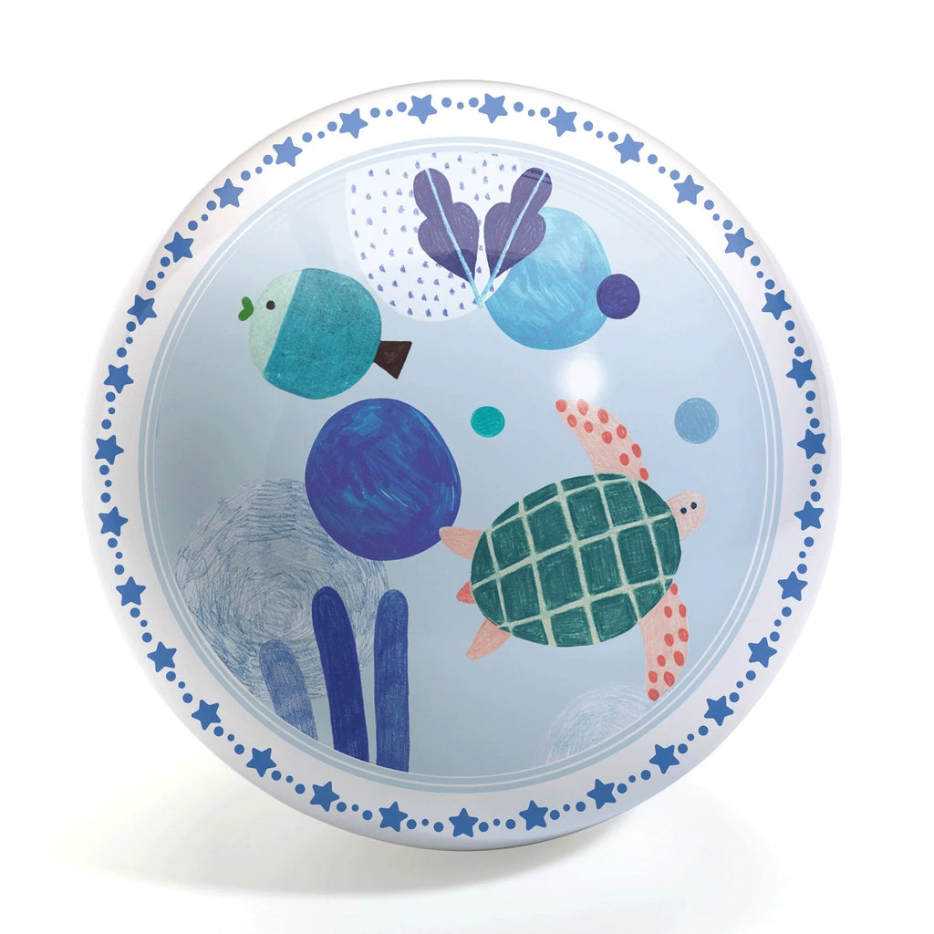 Bola de brincar redonda com ilustração central de uma tartaruga verde e azul rodeada por formas abstratas e elementos marinhos num fundo azul claro. A borda tem um padrão de estrelas azuis.