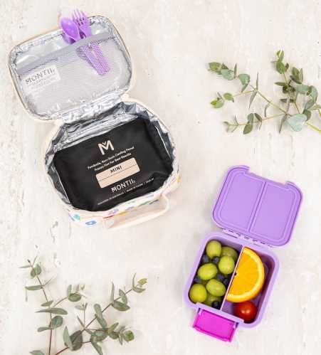 Bolsa de arrefecimento Montii Mini aberta, mostrando o interior isolado e um recipiente de lanche roxo com fruta ao lado.