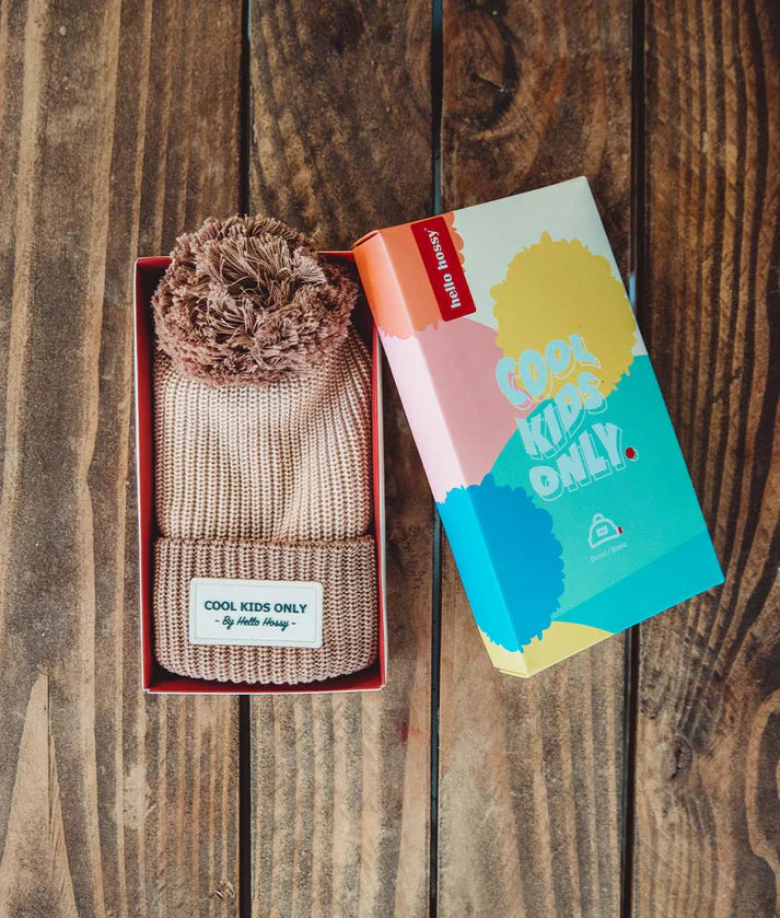Gorro HELLO HOSSY com pompom Coffee dentro da sua caixa "COOL KIDS ONLY", sobre uma superfície de madeira.