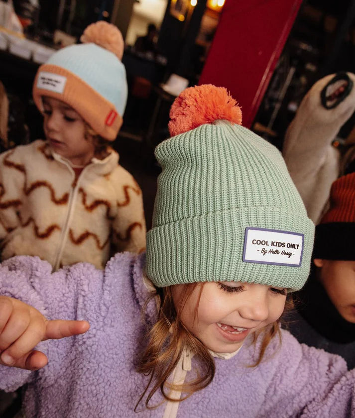 Duas crianças com gorros Hello Hossy, uma com o gorro verde-menta e a outra com um gorro azul claro e laranja.