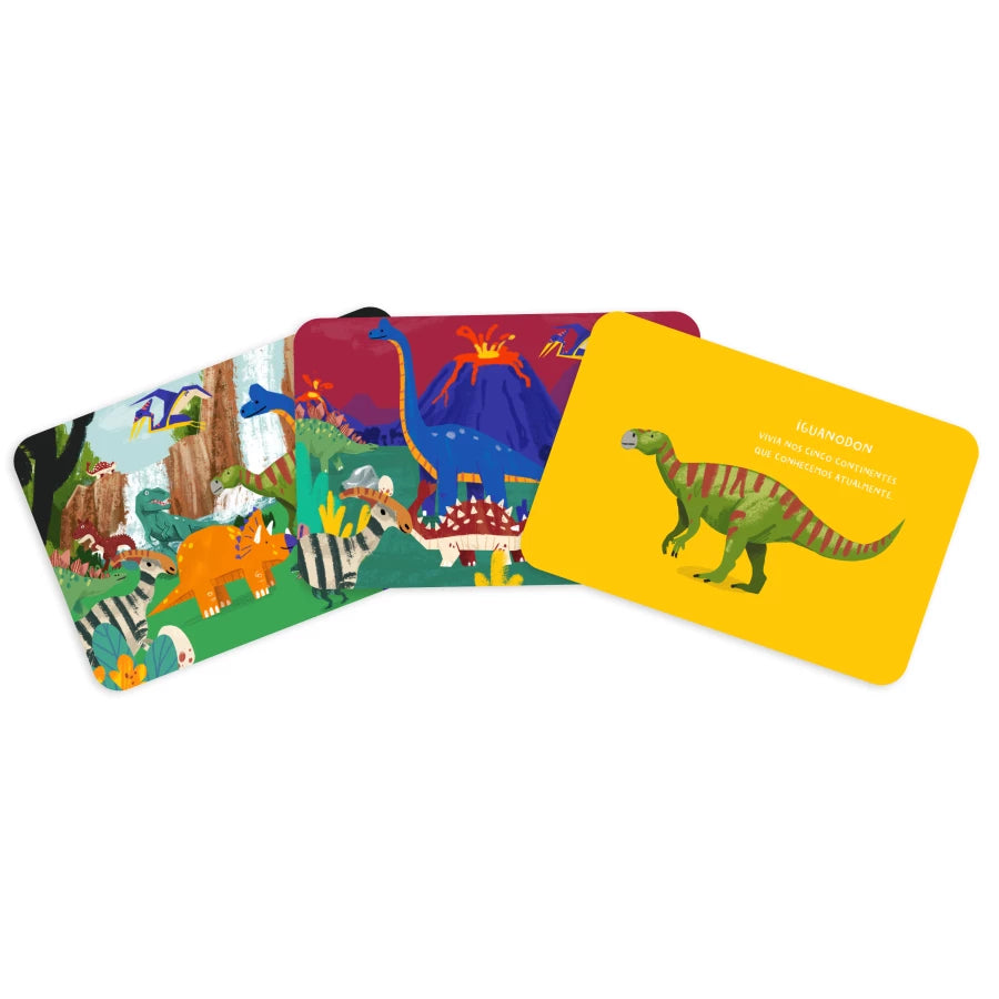 Três cartas do jogo de dinossauros espalhadas: uma com um cenário de selva, outra com um vulcão e uma amarela com a ilustração do Iguandon e uma curiosidade.